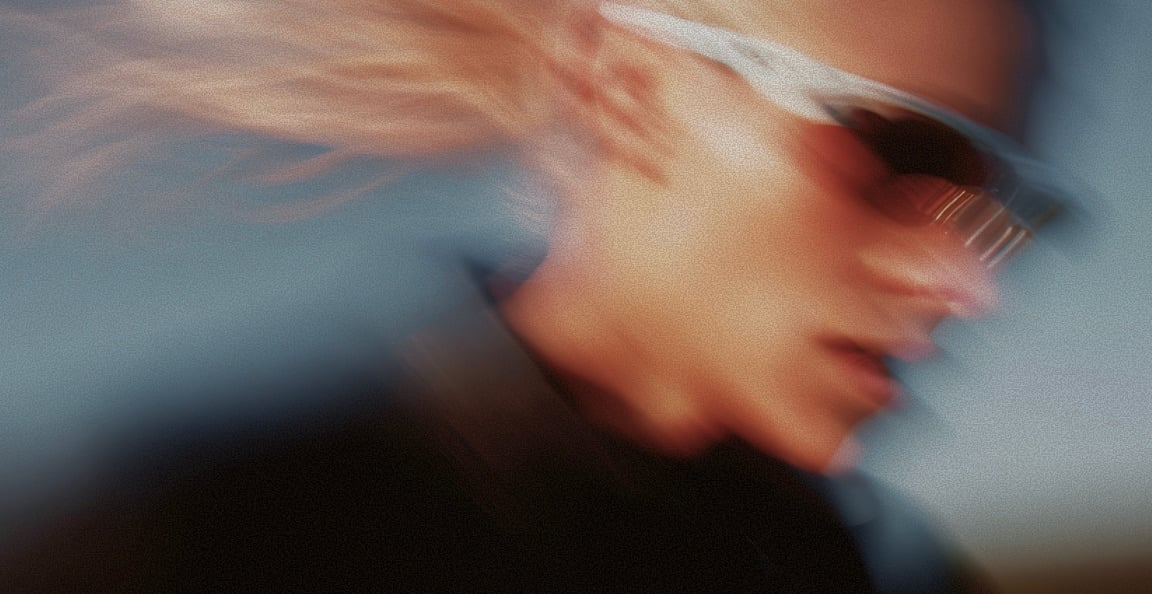 A model in sunglasses, hair streaming across the frame in motion