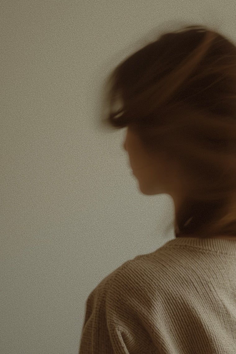 A woman turning away, her hair caught in motion against a pale wall